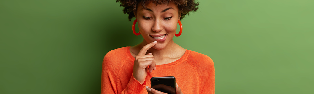 mujer afrodescendiente sobre fondo verde mirando la pantalla de su celular