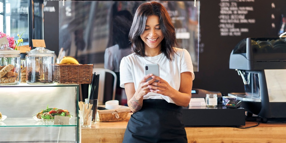 emprendedora barista con smartpone viendo la página web de su negocio