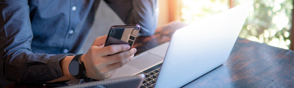 mano masculina sosteniendo smartphone usando ordenador portátil y tableta digital comprarando precios de tiendas online
